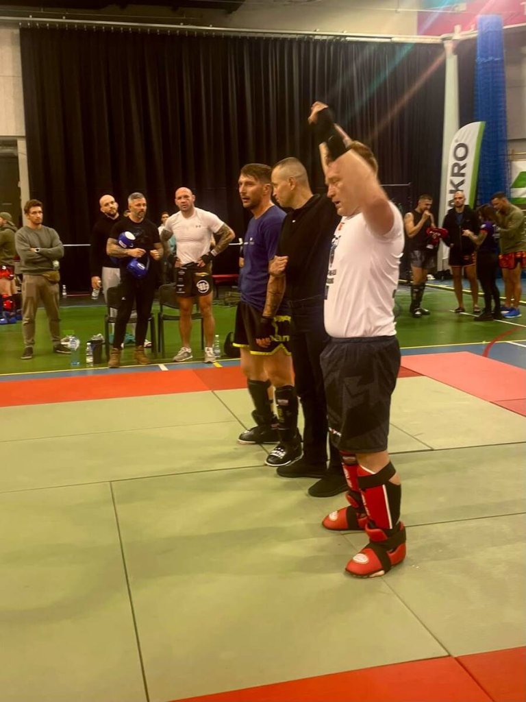 Zawodnik w ochraniaczach z uniesioną ręką po walce kickboxingu na macie